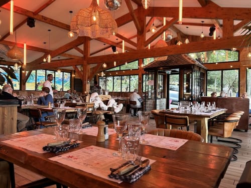 Salle à manger rustique chic de l'Hôtel Saint Roch avec poutres apparentes, luminaires suspendus et tables dressées offrant une vue