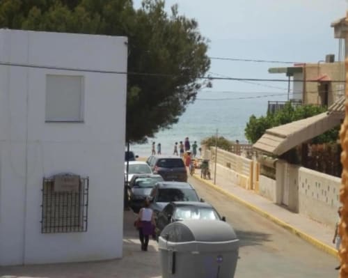 Vue de la rue des Apartamentos Taravilla à Puerto de Mazarrón avec bâtiment blanc, voitures garées et accès à la plage