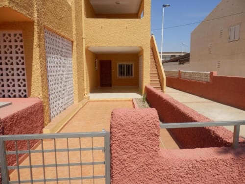 Cour ensoleillée des Apartamentos Taravilla à Puerto de Mazarrón avec bâtiment jaune, murs en terre cuite et balustrades métalliques