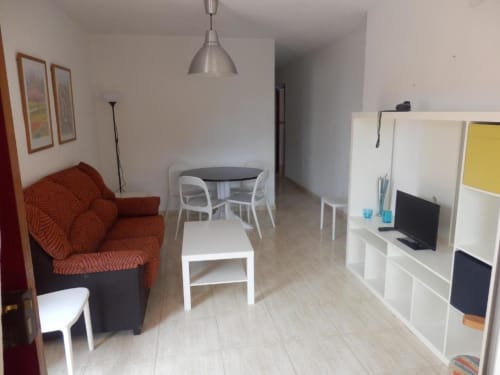 Salon moderne de l'appartement Taravilla avec fauteuil rouge, table à manger, étagères blanches et téléviseur à Puerto de Mazarrón