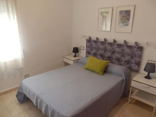 Chambre lumineuse aux Apartamentos Taravilla à Puerto de Mazarrón avec lit double, tête de lit à motifs et oreiller jaune