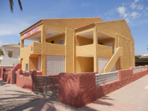 Bright yellow apartment building with red terracotta walls at Apartamentos Taravilla in Puerto de Mazarrón, Spain