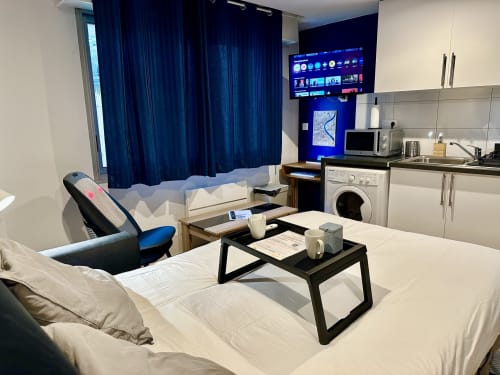 Modern studio apartment in Bordeaux featuring bed, kitchenette, smart TV, washing machine, and blue accent lighting at