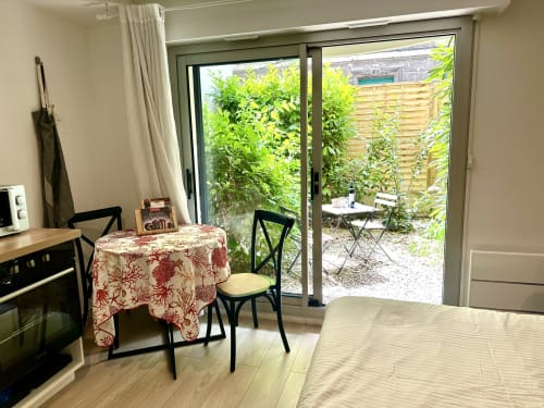 Studio apartment in Bordeaux with dining table, kitchen area, and glass doors opening to private garden courtyard