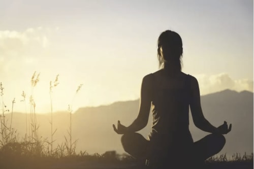 Mulher meditando na natureza em Casa das Jardas, retiro rural em Ladoeiro, Portugal, silhuetada contra o nascer do sol na montanha