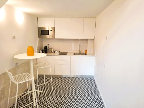 Modern compact kitchen in Newhouse Bari apartment with white cabinetry, built-in microwave, dining table, and geometric floor