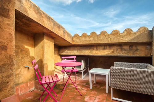 Terrasse rustique des Finques Garcia Enrich à Palafrugell avec mobilier rose et murs en pierre sous un ciel bleu