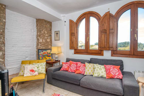 Séjour lumineux aux Finques Garcia Enrich de Palafrugell avec canapé gris, fauteuil jaune, coussins colorés et voûte en bois