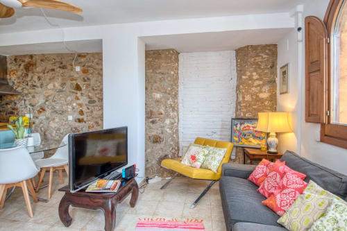 Salon chaleureux à Finques Garcia Enrich, Palafrugell avec murs en pierre, canapé gris, fauteuil jaune et meubles en bois