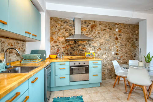 Cuisine moderne turquoise avec comptoirs en bois, mur en pierre et coin repas chez Finques Garcia Enrich, Palafrugell