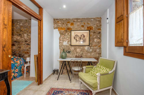 Chambre d'hôte charmante aux Finques Garcia Enrich à Palafrugell avec mur en pierre rustique, fauteuil vert, bureau et bois