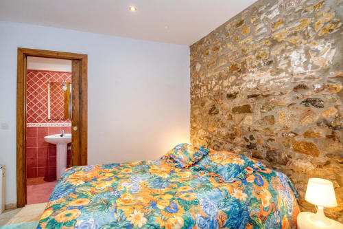 Chambre colorée avec mur en pierre, literie florale et salle de bain attenante à Finques Garcia Enrich à Palafrugell