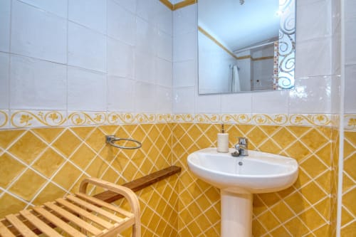 Salle de bains lumineuse aux Finques Garcia Enrich à Palafrugell avec carrelage jaune en losange, lavabo sur colonne et banc en bois