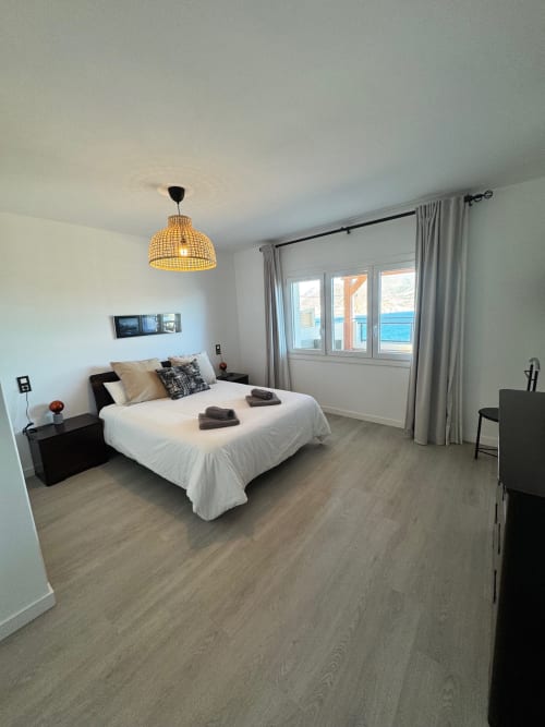 Dormitorio moderno con vista al mar en El Faro De Los Genoveses, Almería. Cama blanca, lámpara colgante tejida, suelo gris y costero
