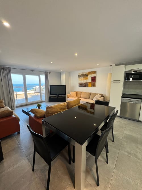 Apartamento moderno con vista al mar, mesa de comedor negra, sofá beige, cocina y balcón con vistas al Mediterráneo en San José.