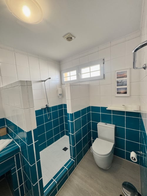 Baño moderno con azulejos en tonos turquesa y blanco, ducha abierta, inodoro y espejo en el apartamento El Faro De Los Genoveses en Almería