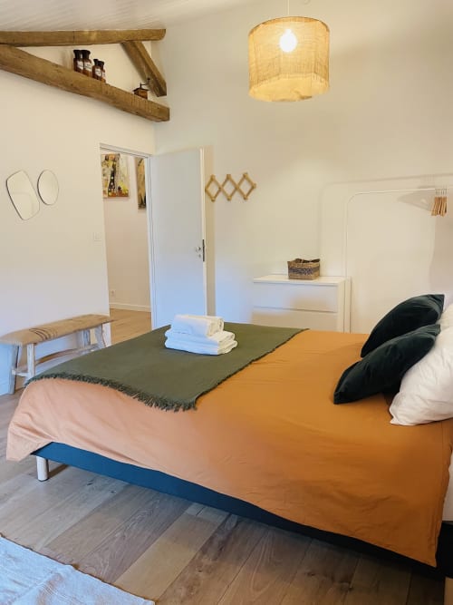 Chambre lumineuse de la Maison Monsieur Léger avec literie orange, poutres en bois et mobilier rustique à Montaut