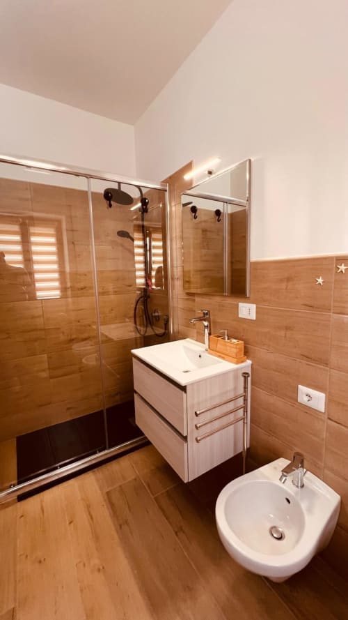 Bagno moderno nell'appartamento La Perla del Sur a Bari con piastrelle in legno, doccia in vetro, vanità bianca e bidet