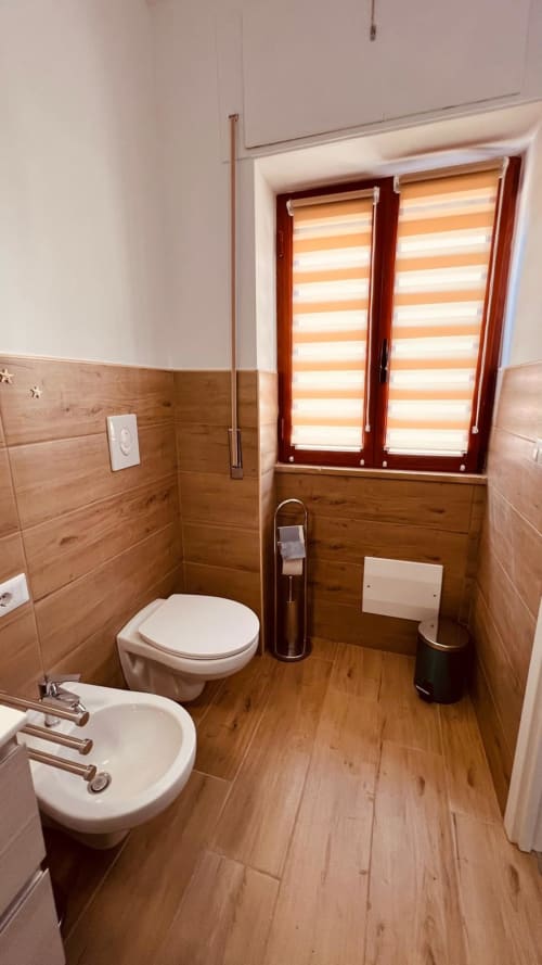 Bagno moderno nell'appartamento La Perla del Sur a Bari con pavimenti in legno, WC e bidet bianchi, persiane a strisce arancioni
