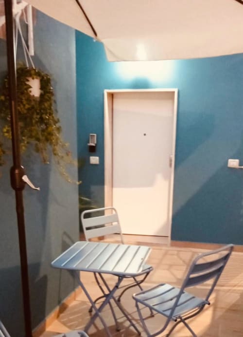 Interno moderno di appartamento con pareti blu, porta bianca, pavimento in legno e sedie metalliche al tavolo in vacanza a Bari