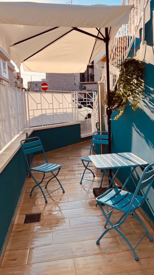 Terrazza soleggiata sul tetto a Bari con sedie blu, vela ombreggiante e vista sulla città - Appartamento vacanze Bari