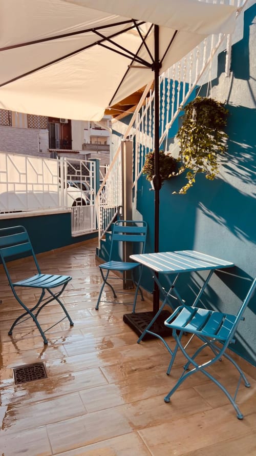 Terrazza soleggiata di Bari con arredamento blu, ombrellone e pianta in vaso con vista sulla città