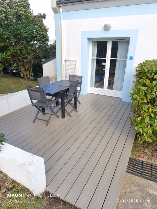 Terrasse composite moderne avec mobilier de salle à manger extérieure surplombant l'appartement Belle Île aux façades bleu et blanc