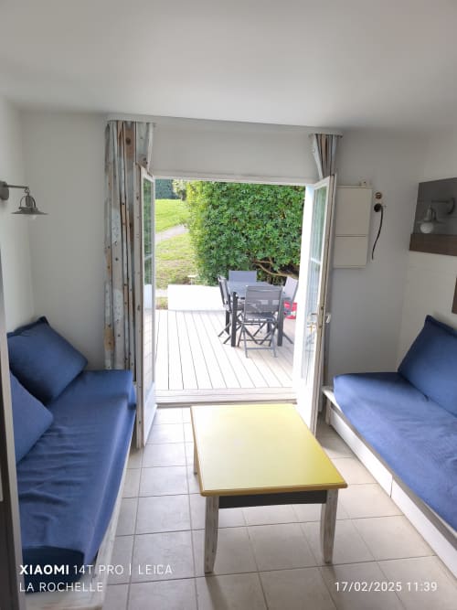 Lumineux salon d'appartement avec sièges bleus, table jaune et portes ouvertes sur la terrasse du jardin à Belle Île en Mer
