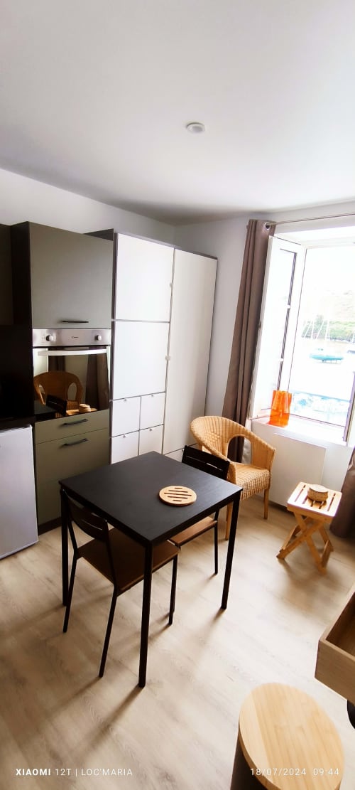 Espace cuisine-salle à manger moderne à Loc'Maria Belle Île en Mer avec table noire, chaise en rotin et vue sur mer