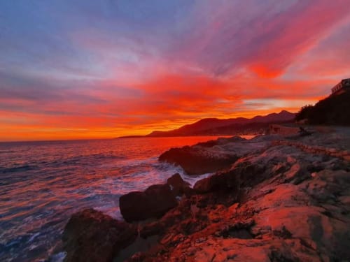 Tramonto spettacolare sulla spiaggia rocciosa dell'appartamento TuffonelBlu a Ventimiglia con cielo arancione vivido e vista sul mare