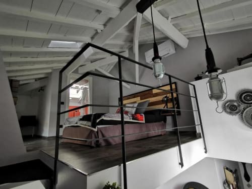 Camera da letto in stile loft moderno con letto a baldacchino in metallo nero, travi a vista bianche e lampade a sospensione nell'appartamento di Ventimiglia