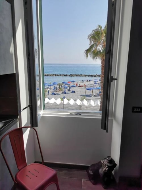 Porta in vetro aperta sul balcone dell'appartamento TuffonelBlu a Ventimiglia con vista sul mare Mediterraneo, ombrelloni e palme