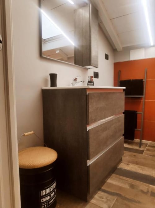 Bagno moderno in appartamento a Ventimiglia con vanità scura, mobile specchio e parete accent arancione