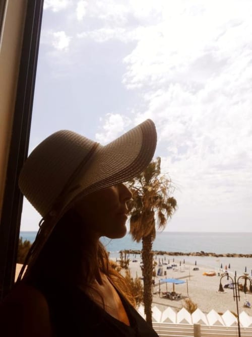 Donna con cappello di paglia che ammira la spiaggia di Ventimiglia e il Mar Mediterraneo dall'appartamento vista mare TuffonelBlu