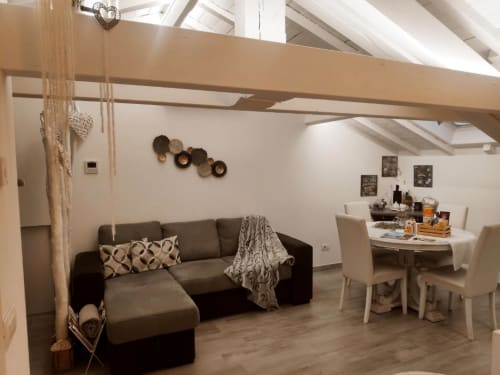 Luminoso loft a Ventimiglia con divano grigio, zona pranzo, travi a vista e piatti decorativi