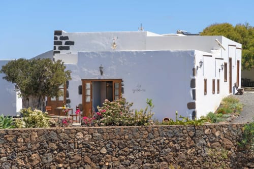 Finca de La Geria whitewashed villa in Yaiza with wooden doors, stone walls, and flowering plants under blue sky