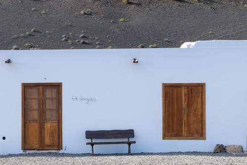 White exterior wall of Finca de La Geria in Yaiza with wooden doors, bench, and volcanic terrain above