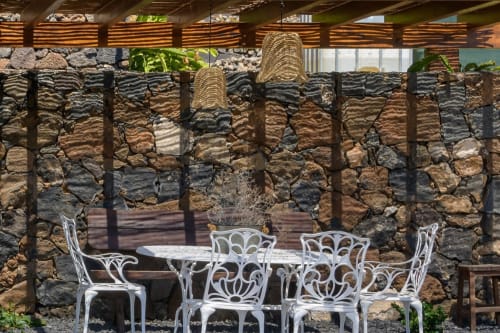 White ornate chairs at dining table in shaded courtyard with stone walls at Finca de La Geria, Yaiza