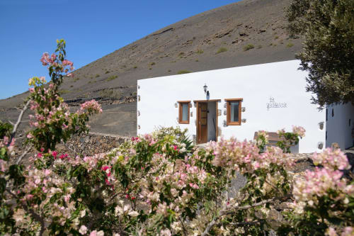Finca de La Geria hotel in Yaiza with white-washed building, wooden doors, pink flowers, and volcanic hillside landscape