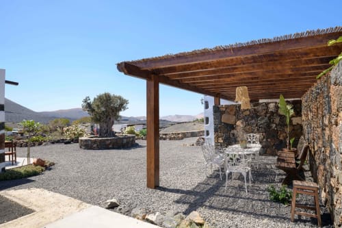 Finca de La Geria courtyard with wooden pergola, stone walls, white seating, and volcanic landscape views in Yaiza