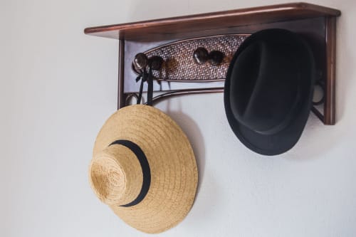 Estante de madera montado en pared con ganchos sosteniendo un sombrero de paja y un sombrero negro en Finca de La Geria