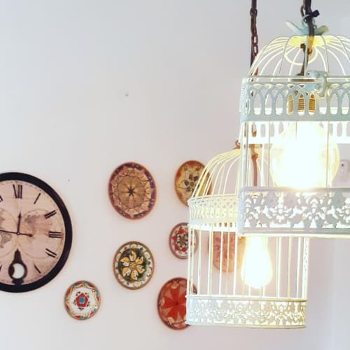 Exposición decorativa en Finca de La Geria con reloj vintage, lámpara colgante tipo jaula ornamental y platos de cerámica