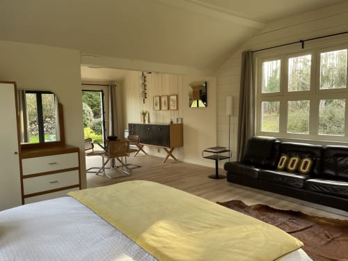 Spacious cottage bedroom at Clairseine with garden views, featuring bed, black leather sofa, wooden desk and large windows