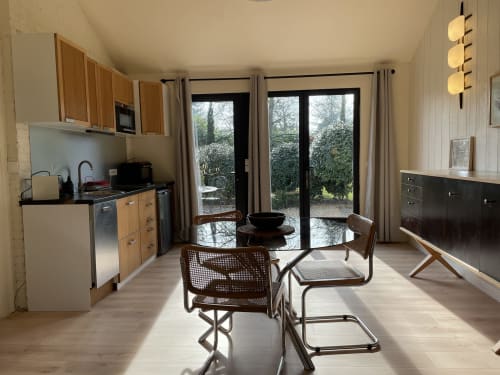 Modern cottage kitchen and dining area at Clairseine with garden view, wooden cabinets, dining table, and glass doors opening