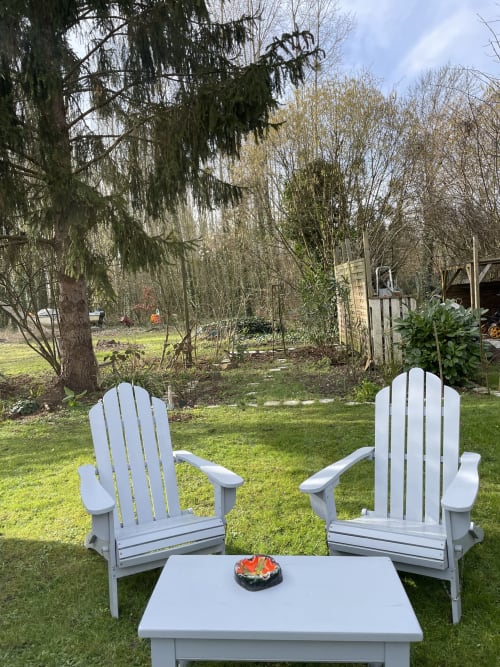 Two white Adirondack chairs facing a garden with trees at Clairseine cottage in Tournedos-sur-Seine, France