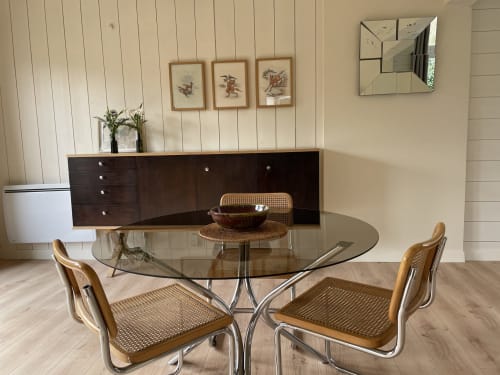 Modern dining room with round glass table, rattan chairs, dark wood sideboard, and garden views at Clairseine cottage