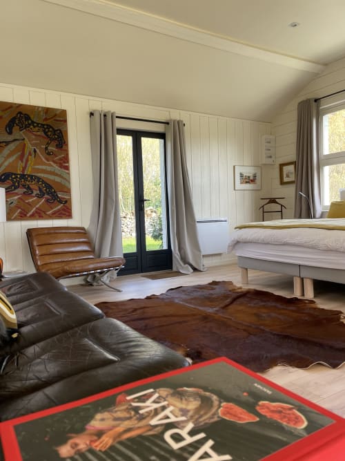 Modern cottage bedroom at Clairseine with leather chair, bed, garden view doors, and colorful leopard artwork