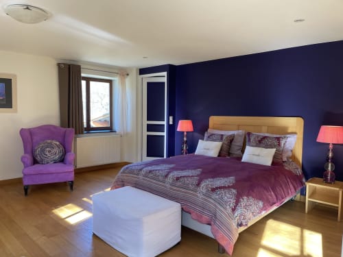 Chambre spacieuse du gîte Entre Terre Et Ciel à Rémuzat avec mur d'accent bleu marine, tête de lit dorée et fauteuil violet