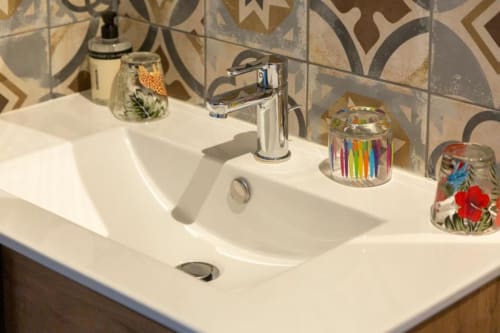 Modernes weißes Doppelwaschbecken mit Chromarmatur und farbenfrohen Dekorationsgefäßen im Badezimmer des Gîte Le Penty in Concarneau
