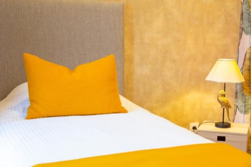 Helles Schlafzimmer im Gîte Le Penty mit weißem Bett, gelbem Kissen, Nachttischlampe und Gartenblick